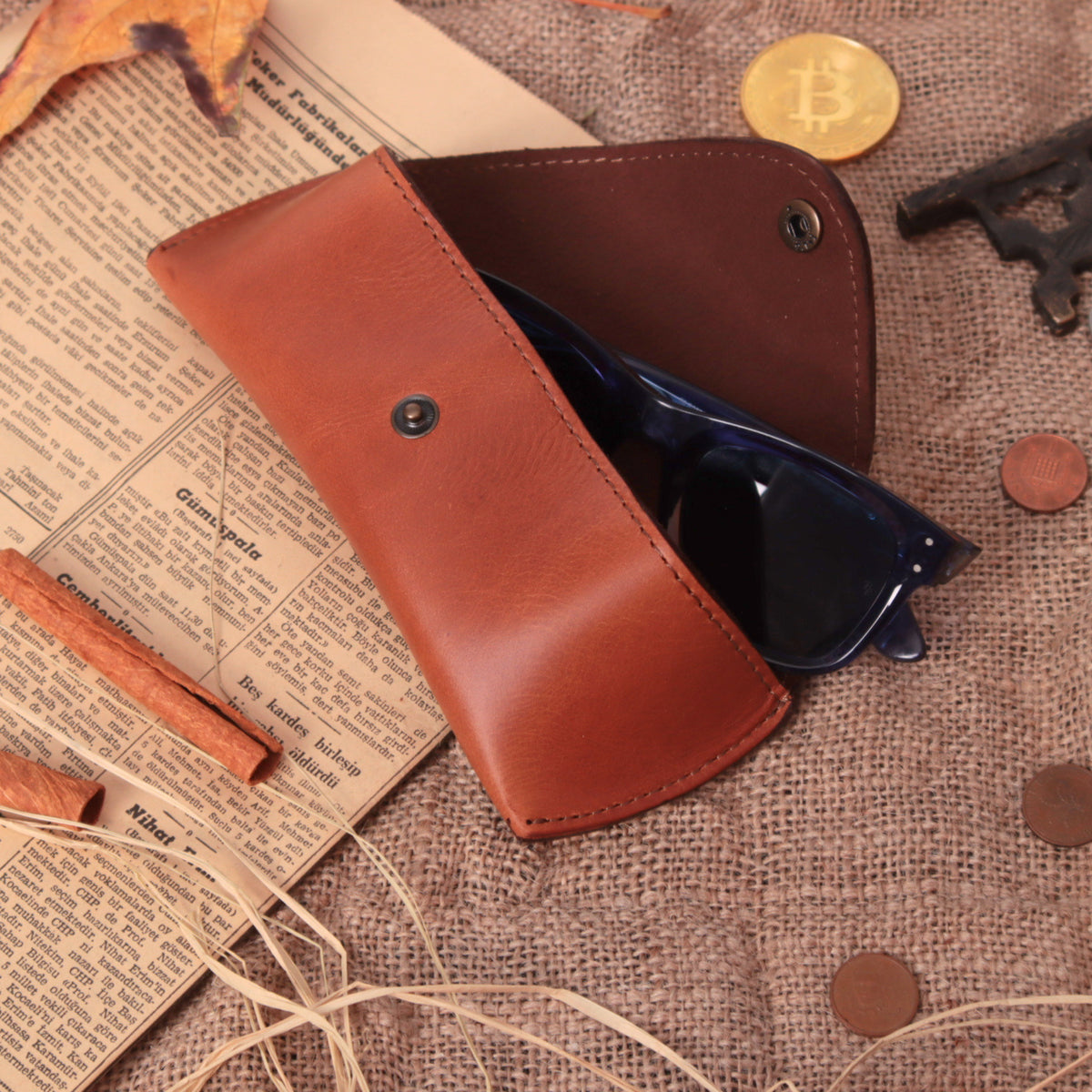 Open chestnut leather sunglasses case holding black frames