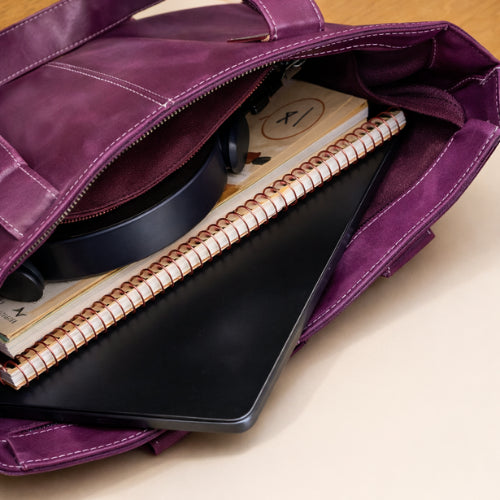 Open purple leather tote holding a laptop, notebook, and everyday essentials