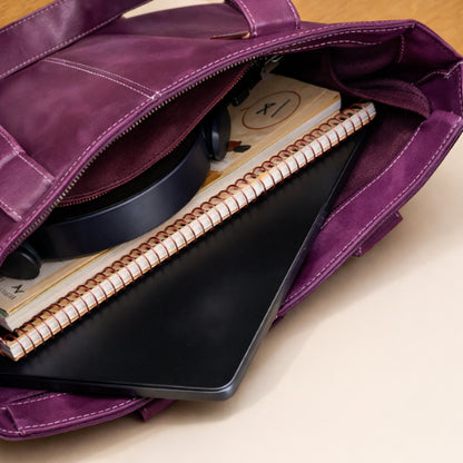 Open purple leather tote holding a laptop, notebook, and everyday essentials
