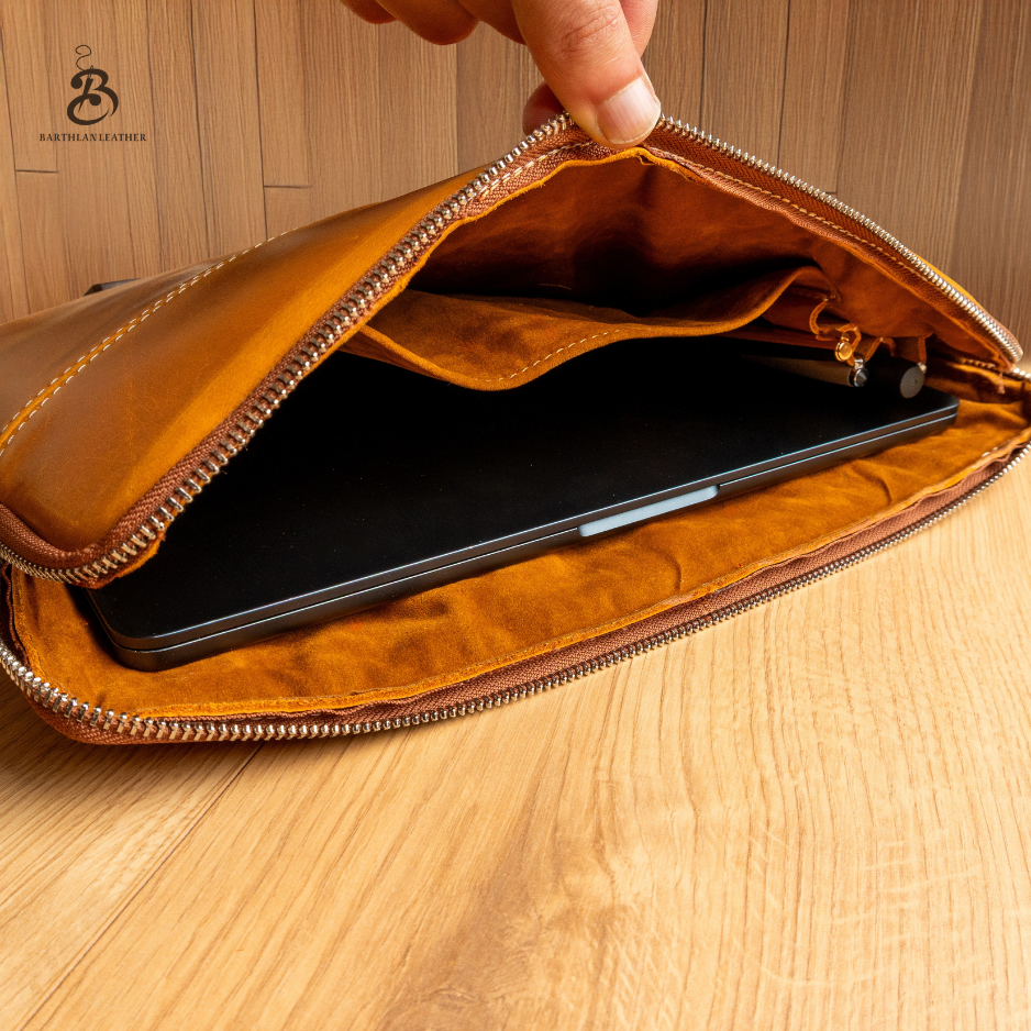 Open camel leather laptop bag showing device compartment and zip pocket