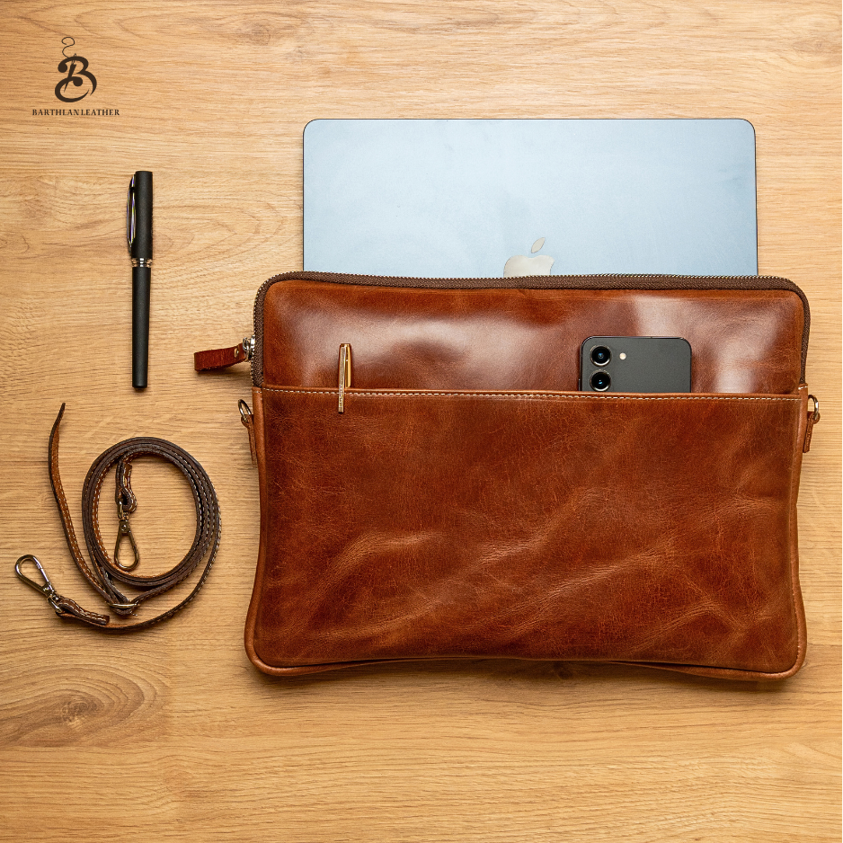 Open chestnut laptop bag with MacBook, phone, pen, and shoulder strap
