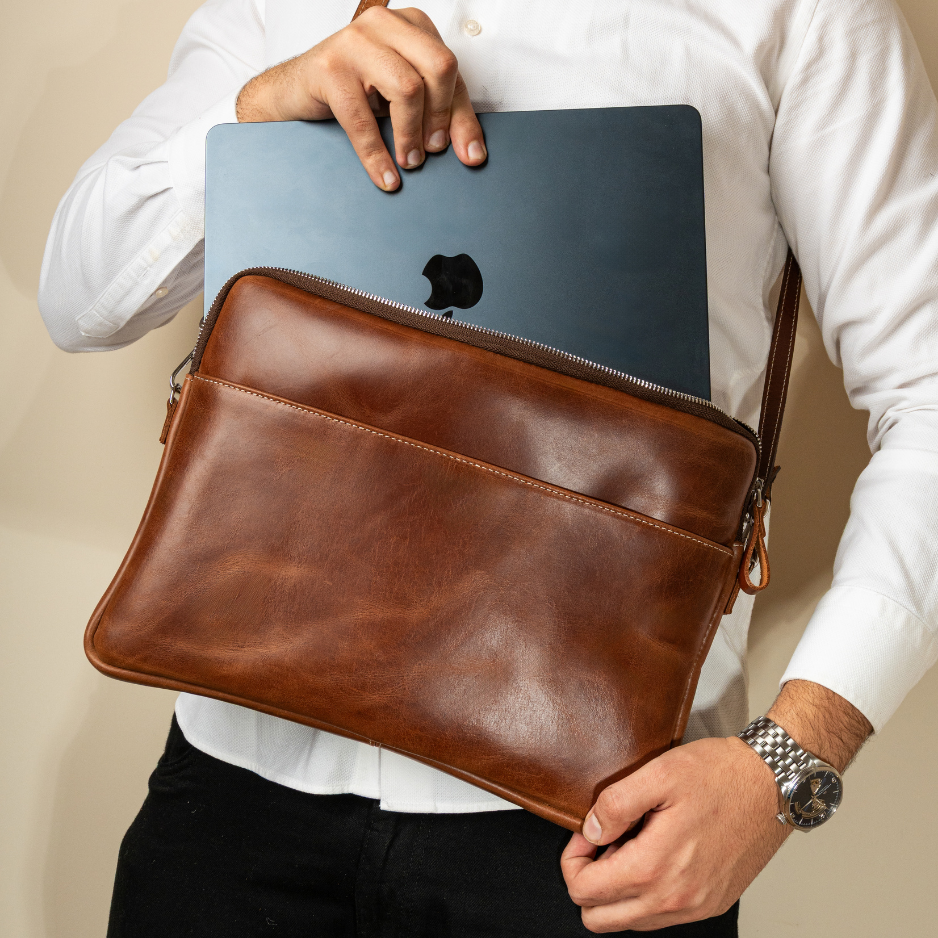 Man sliding a MacBook into a chestnut full grain leather laptop bag