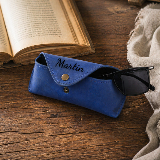 Blue leather sunglasses case personalized with Martin beside eyeglasses