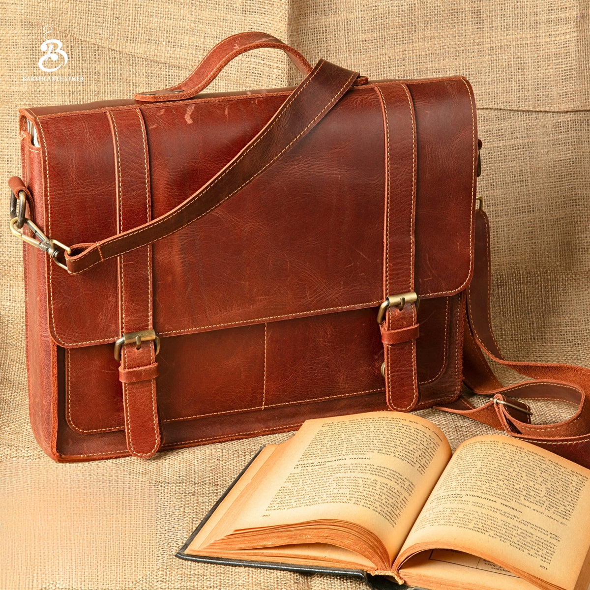 Chestnut leather briefcase with shoulder strap beside an open book