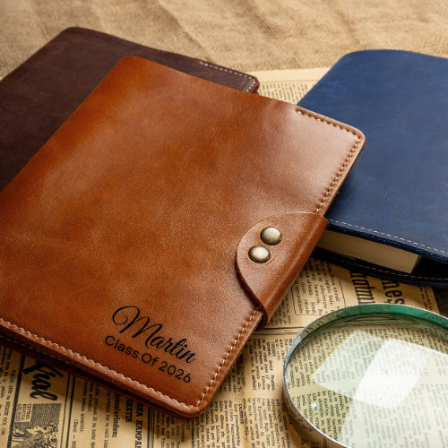 Chestnut monogrammed A5 leather portfolio in front of blue and dark brown covers
