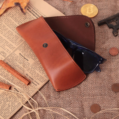 Open chestnut leather sunglasses case holding black frames